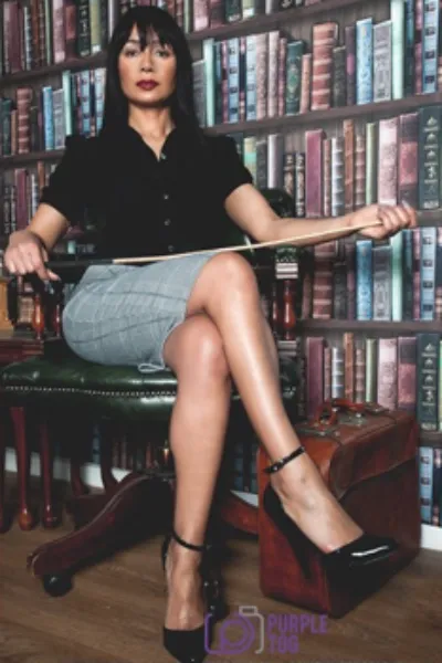 Mistress Mera holding a cane in the library