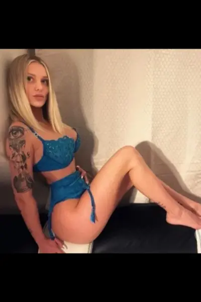 Tattooed busty blonde escort in blue lingerie